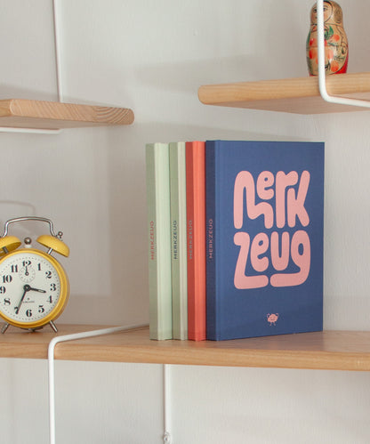 Merkzeug Notizbuch im Regal, alle Titel, blauer Titel mit rosa Schrift, Stilleben